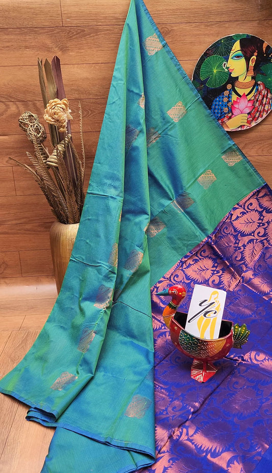 A soft silk saree with borderless design, draped over a chair, displaying its green body with golden accents and a red border at the bottom.