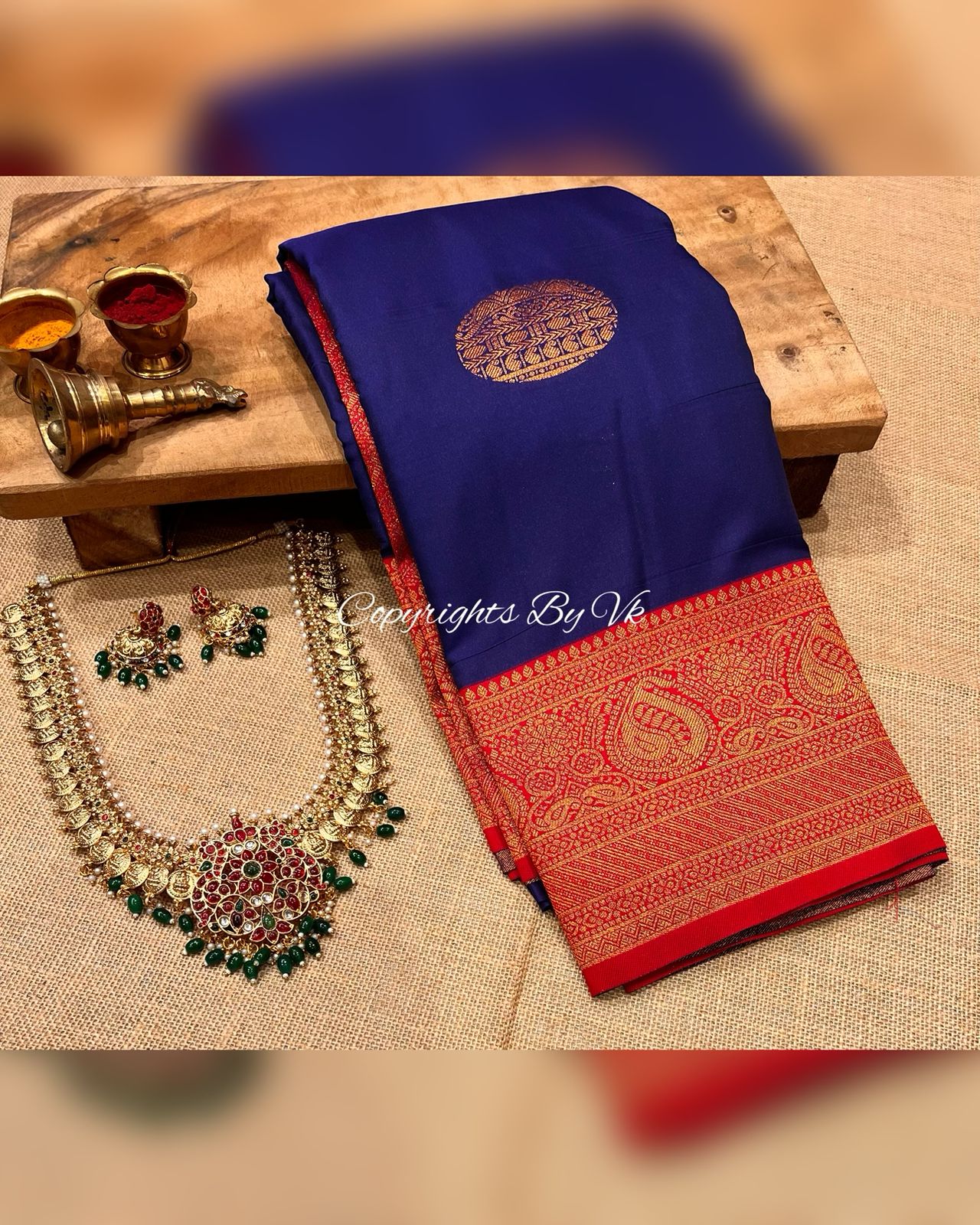 Navy blue and red pattu saree with intricate border designs, displayed on a wooden surface with jewelry and accessories.
