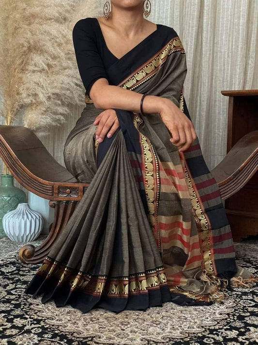 A woman sitting on a chair, wearing a mud gray Narayanpeth Mercerised cotton saree with traditional borders.