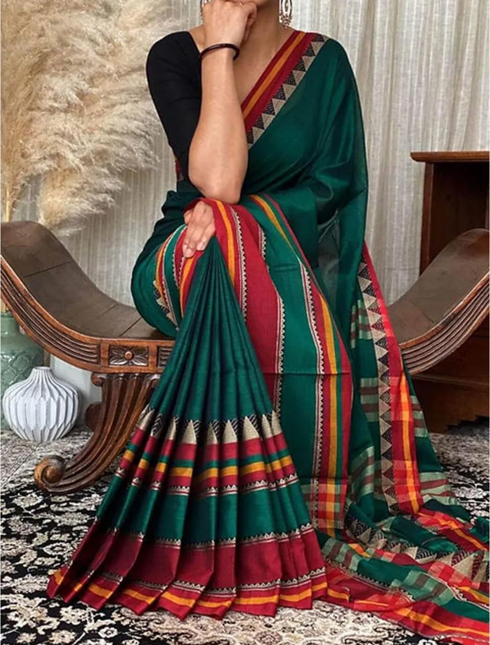 A woman sitting on a chair, draped in a deep sea green pure Narayanpeth mercerised cotton saree with traditional borders.