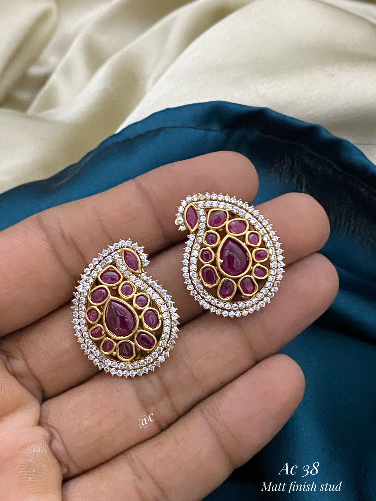 Ornate earrings with gemstones held between fingers against a blue fabric background