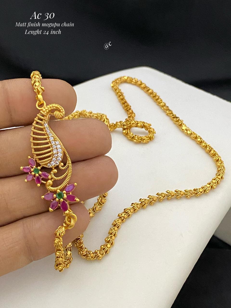 Gold necklace with a decorative pendant held by a hand on a white surface.