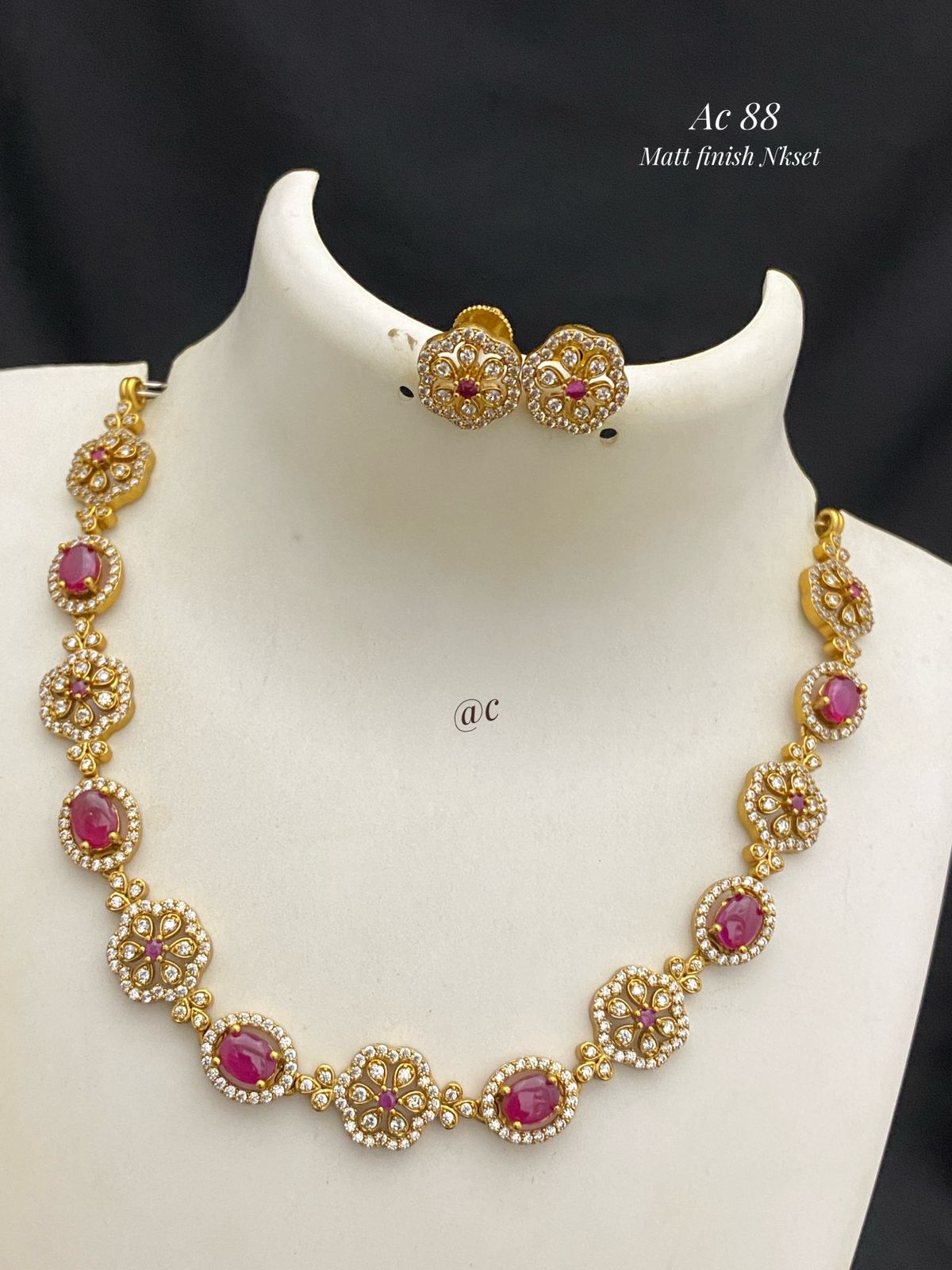 Gold necklace with red gemstones on a mannequin bust against a black background