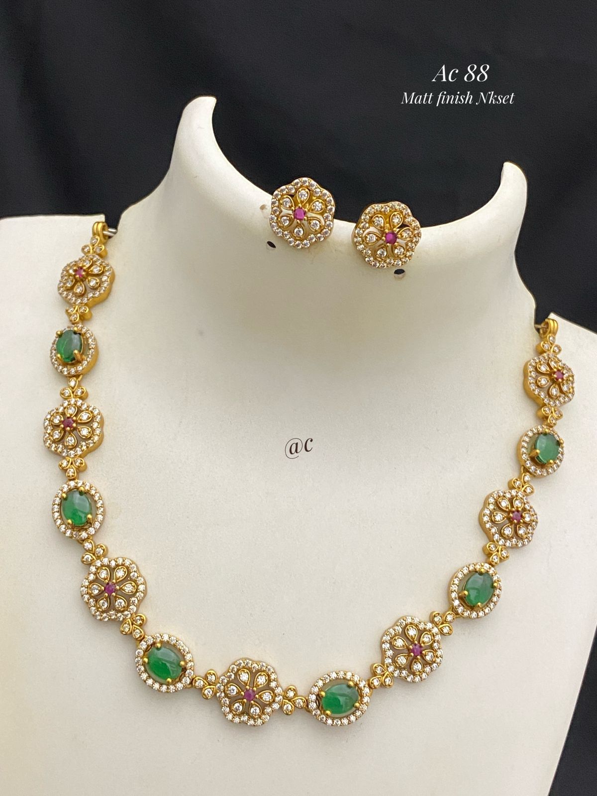 Gold necklace with emerald and ruby stones on a mannequin bust.
