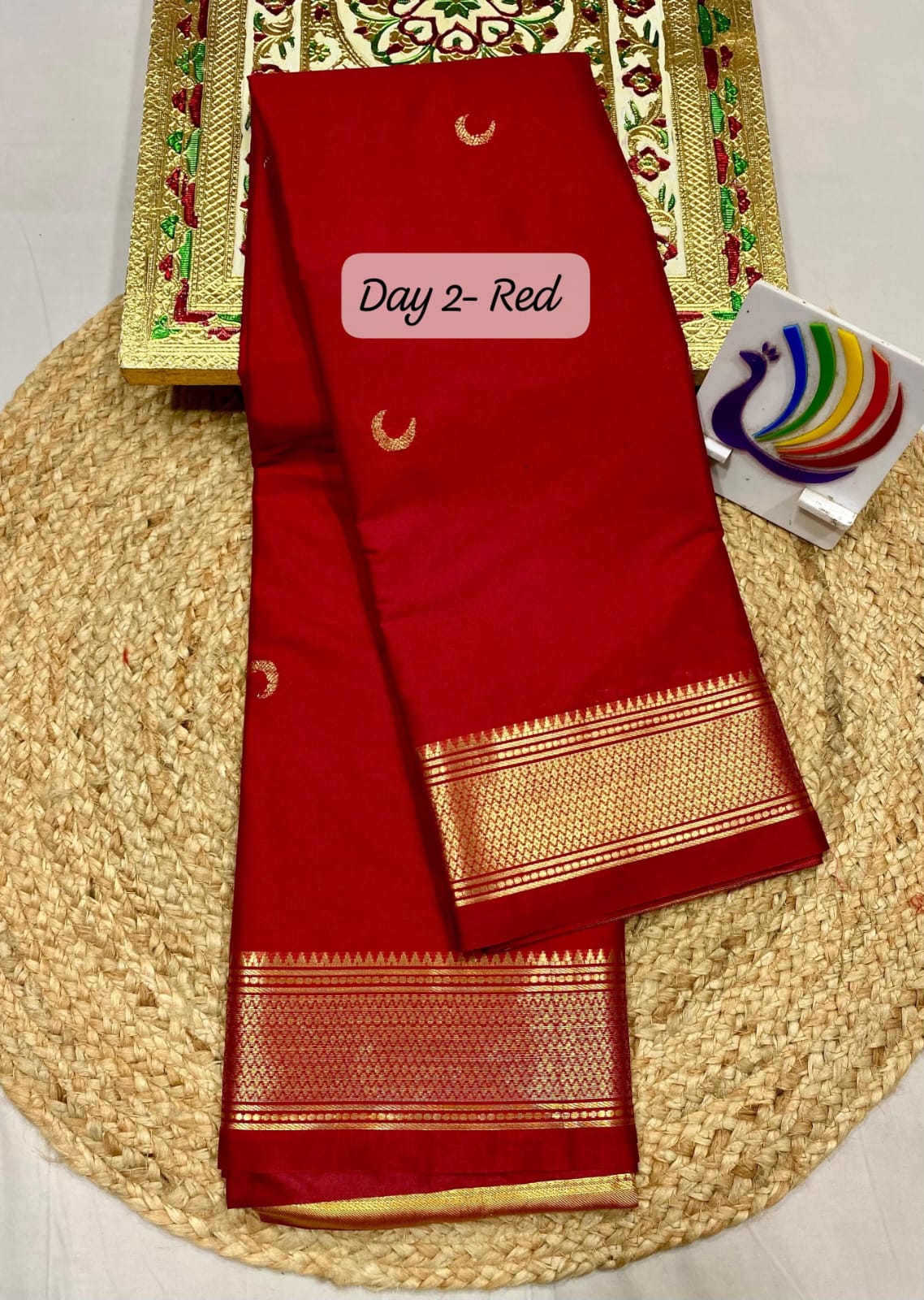 Red saree with gold border on a woven mat, with a visible brand tag.