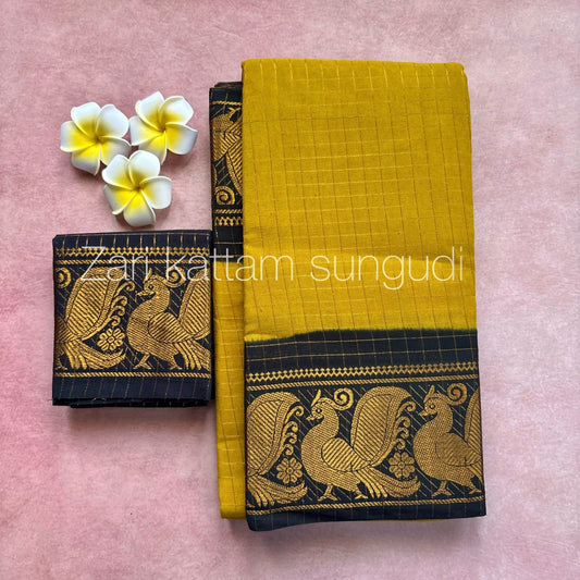 A mustard yellow and black Madurai sungudi cotton saree with an annam design, displayed alongside yellow flowers on a pink background.
