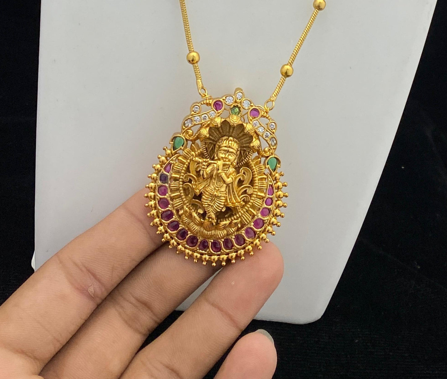 Gold pendant with intricate design held by a hand against a white background