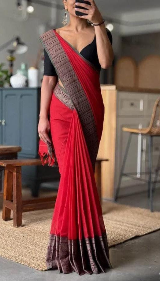 Person wearing a red saree with black border indoors.