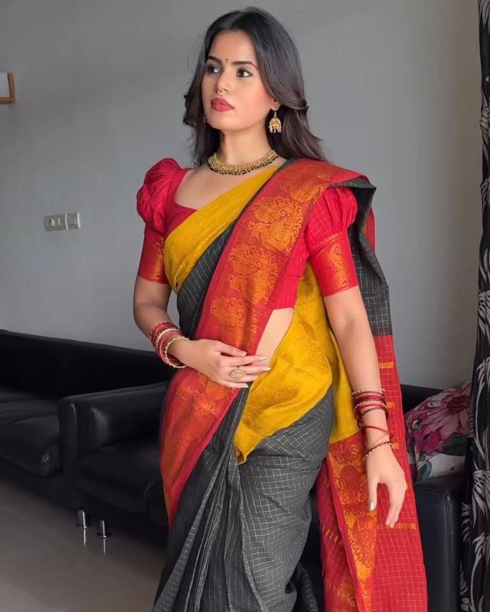 Woman wearing a traditional saree with a red, yellow, and gray pattern in an indoor setting.