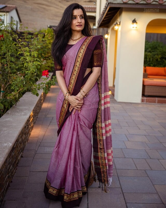 Woman in a pink saree with gold border standing outdoors.