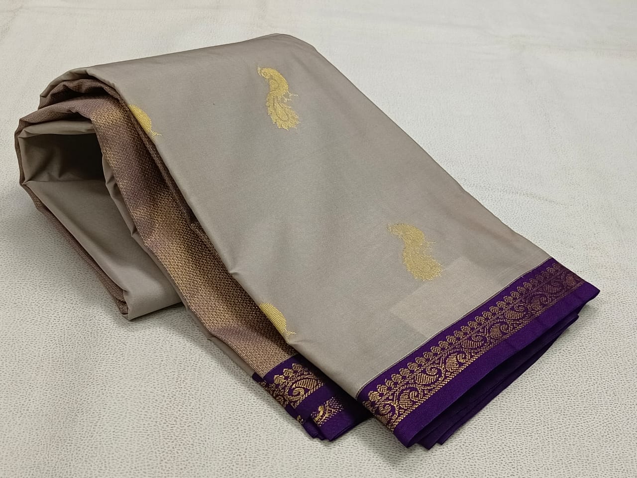 Folded fabric with gold and purple patterns on a light gray background