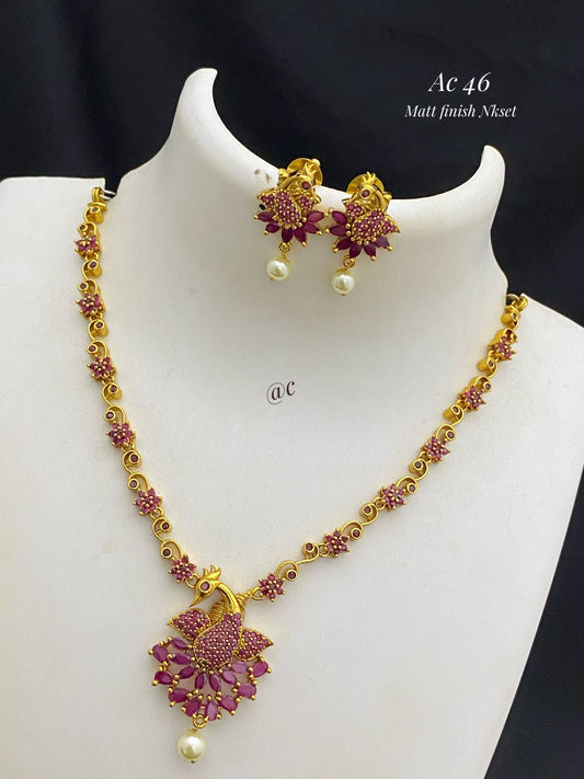 Gold necklace and earrings with pink and red stones on a mannequin.