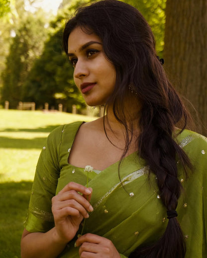 Woman in a green saree standing outdoors with trees in the background