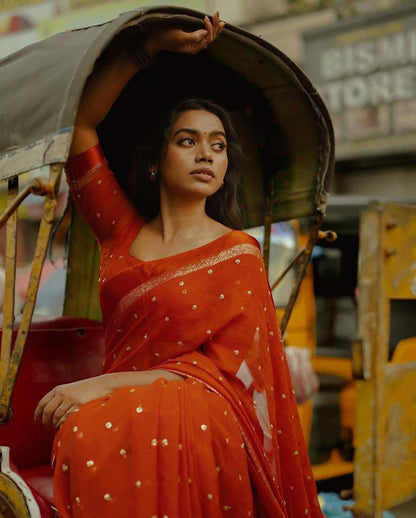 Woman in a red saree sitting inside an auto-rickshaw with blurred background