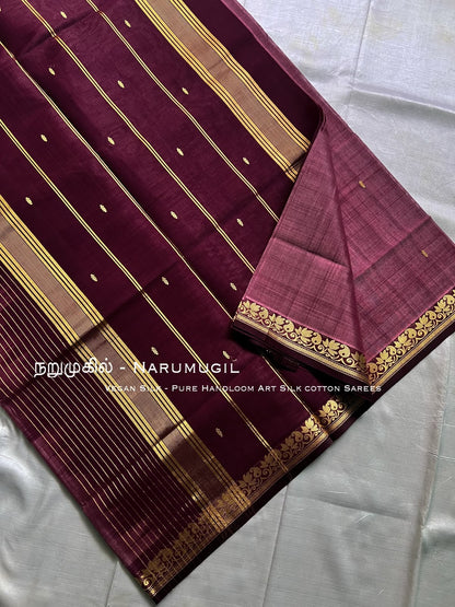 A deep maroon silk saree with gold zari stripes and motifs, folded to display its border, on a white fabric background.  