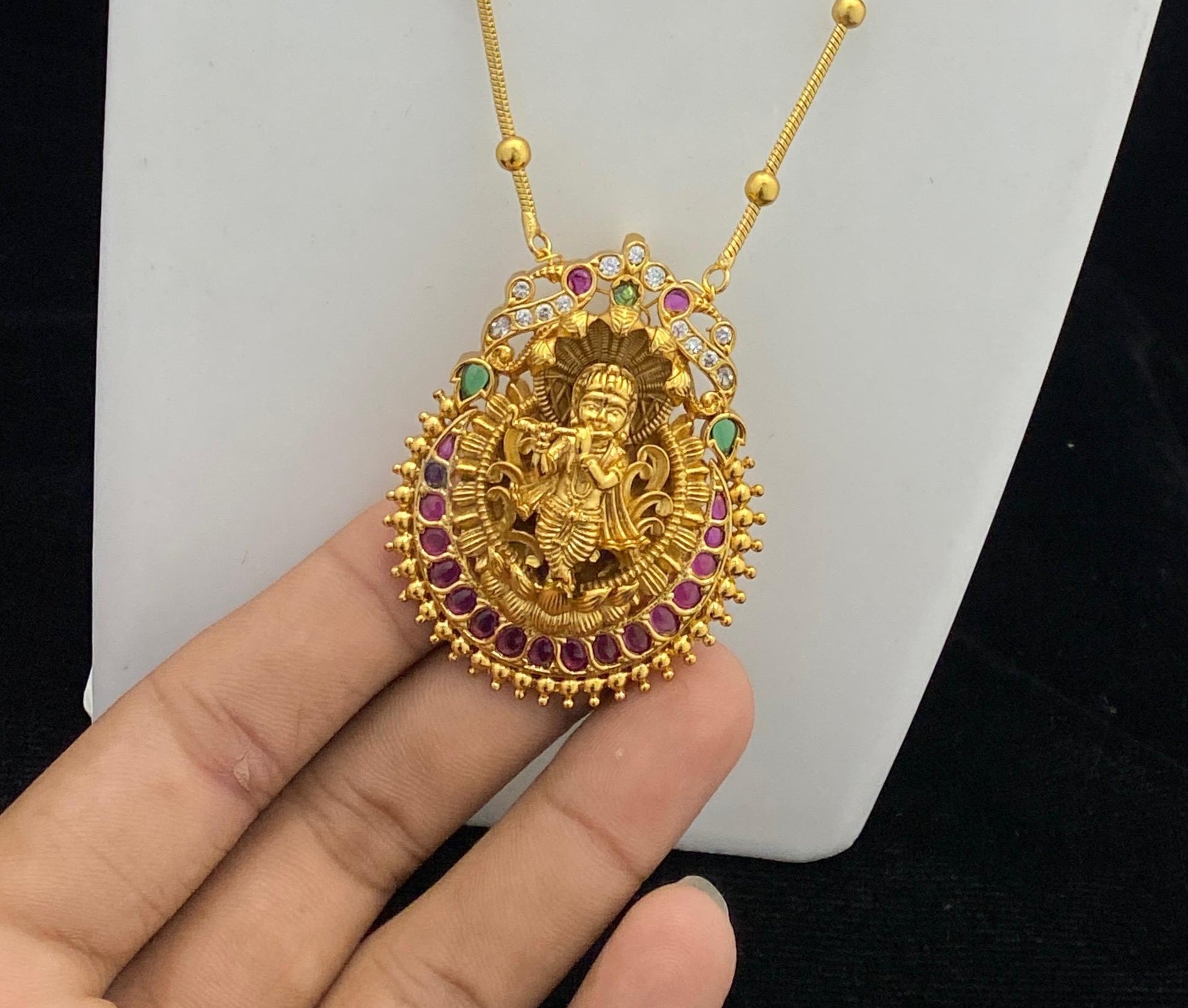 Gold pendant with intricate design held by a hand against a white background