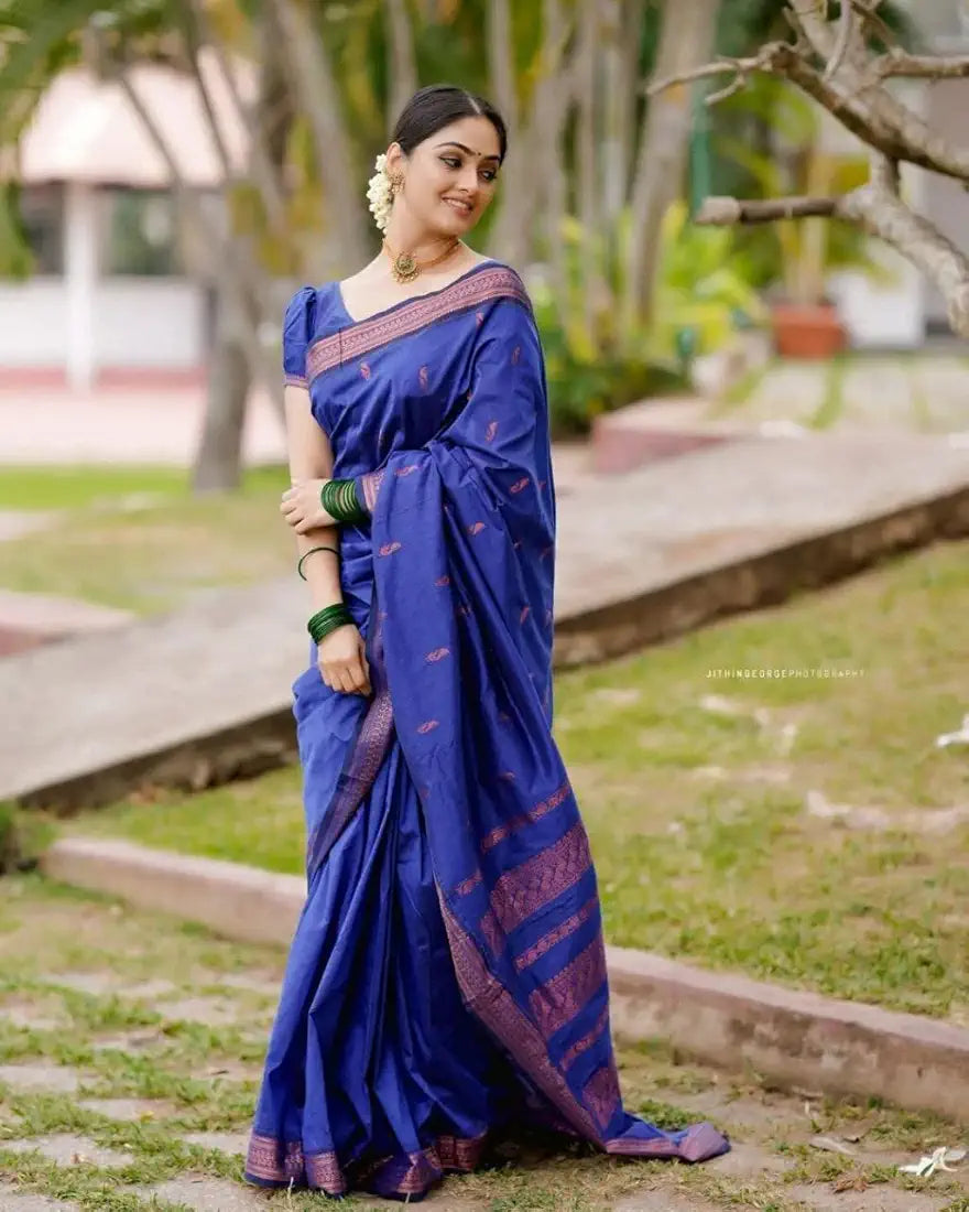 Woman in a blue saree standing outdoors with greenery in the background