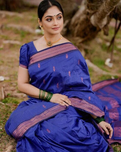 Woman wearing a blue saree with pink border sitting outdoors.